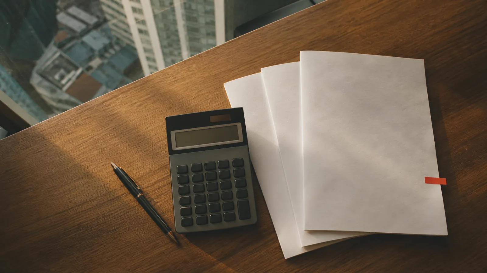 A calculator, pen and blank quotation documents on a desk, Kuala Lumpur skyline beyond